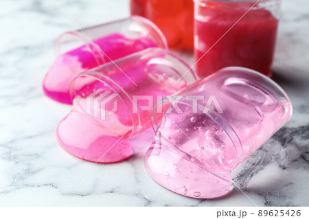 Overturned plastic containers with bright slimes on marble background, closeup 89625426