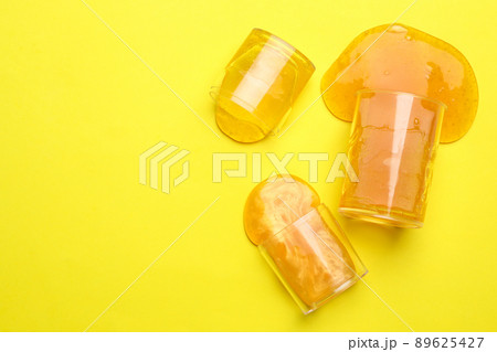 Overturned plastic containers with bright slimes on yellow background, top view. Space for text 89625427