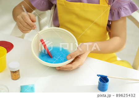 Little girl mixing ingredients with silicone spatula at table, closeup. DIY slime toy Little girl mixing ingredients with silicone spatula at table, closeup. DIY slime toy 89625432