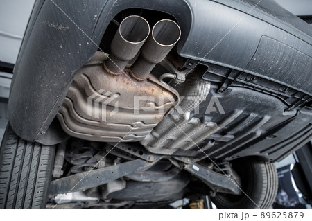 Close-up detail bottom view of car part metal exhaust muffler pipe with rusty stains. Lifted vehicle check-up maintenace service, repair and fix at automotive workshop 89625879