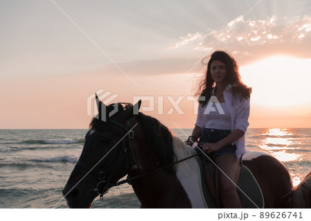 Woman in summer clothes enjoys riding a horse on a beautiful sandy beach at sunset. Selective focus  89626741