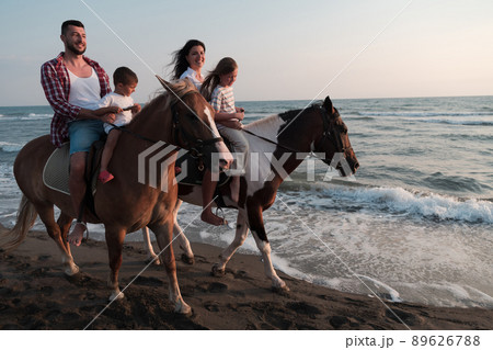 The family spends time with their children while riding horses together on a sandy beach. Selective focus The family spends time with their children while riding horses together on a sandy beach. Selective focus 89626788