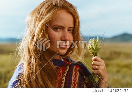 red-haired with freckles on the face of the girl flirtatiously looks into the camera holding a bouquet of wild flowers red-haired with freckles on the face of the girl flirtatiously looks into the camera holding a bouquet of wild flowers 89629432