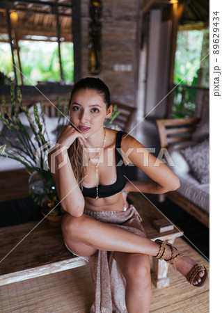 sitting on a bench in a hotel room the girl threw her foot on her leg and plunged her chin with her hand sitting on a bench in a hotel room the girl threw her foot on her leg and plunged her chin with her hand 89629434