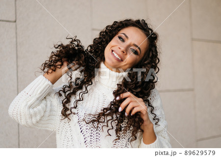 Smiles and plays with her curly brunette hair with a charming white-toothed smile. close-up 89629579