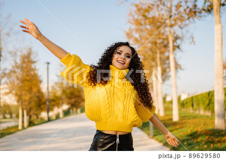 Joyful girl in a bright yellow sweater of large knitting spread her arms to the sides smiling broadly in the park on the track 89629580