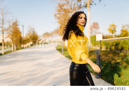 On the park path in autumn comes a girl in a bright yellow sweater her black curls are spread over her shoulders 89629582
