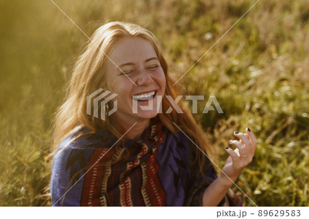 on the steppe grass sits a girl of natural natural beauty with long red hair in an ethno cape and contagion laughs 89629583