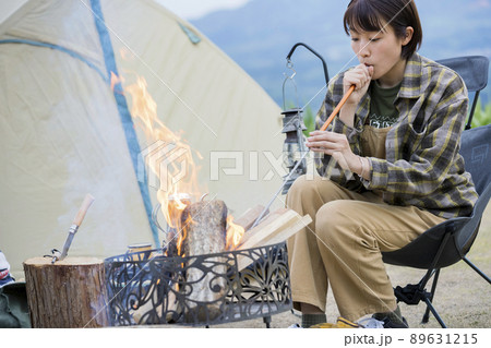 焚火で火吹き棒を使う若い女性　ソロキャンプ　 89631215