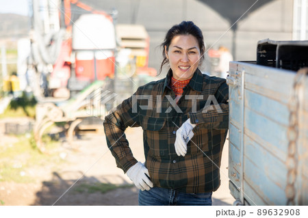 Portrait of positive female tractor driver in farm backyard Portrait of positive female tractor driver in farm backyard 89632908