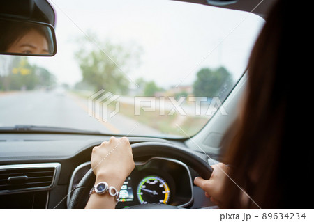 Unrecognizable female driver using left hand grabs on the steering wheel while driving on the road, woman driving a modern electric car EV in beautiful sunlight on the road. Safety driving concept. 89634234