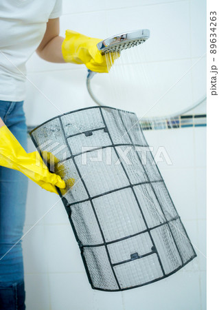 Asian woman cleaning a dirty and dusty air conditioning filter in her house. Housewife removing a dusty air conditioner filter. 89634263