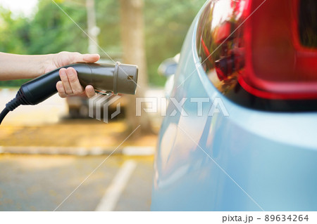 Unrecognizable Asian woman holding AC type 2 EV charging connector at EV charging station, woman preparing an EV - electric vehicle charging connector for recharge a vehicle. 89634264
