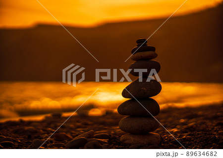 Pebble pyramid silhouette on the beach. Sunset with sea in the background. Zen stones on the sea beach concept, tranquility, balance. Selective focus 89634682