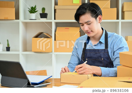 Hard-working Asian man packing a delivery product, writing a customer name and address 89638106