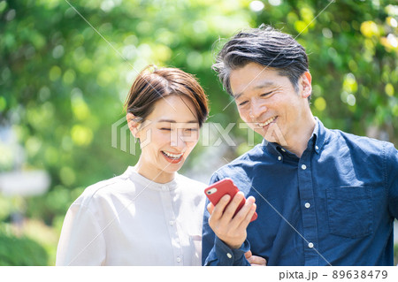 スマホを見るミドル夫婦（カップル・屋外・新緑・笑顔） 89638479