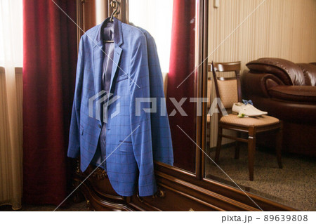 The groom's blue jacket on a hanger on a vintage wardrobe. Groom's morning, wedding details, preparation for the wedding ceremony. 89639808