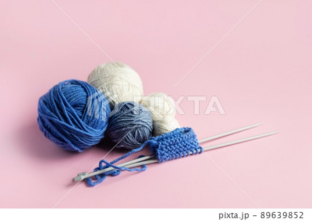 Blue and white knitted wool on a pink background with knitting needles for knitting warm clothes, hobbies Blue and white knitted wool on a pink background with knitting needles for knitting warm clothes, hobbies 89639852