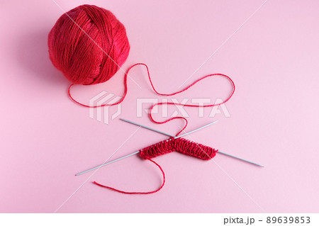Red knitted wool on a pink background with knitting needles, hobby Red knitted wool on a pink background with knitting needles, hobby 89639853