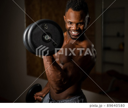 Attractive african american man smiling and doing exercise with dumbbells.  89640580