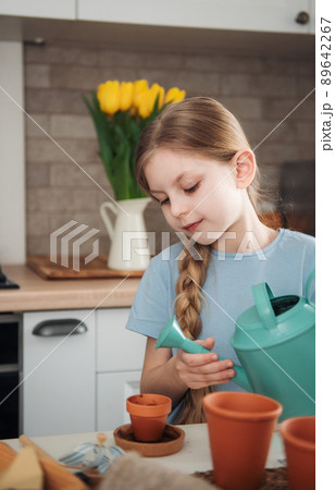 Little girl sitting at the table at home, sowing seeds into flower pots. Little girl sitting at the table at home, sowing seeds into flower pots. 89642267