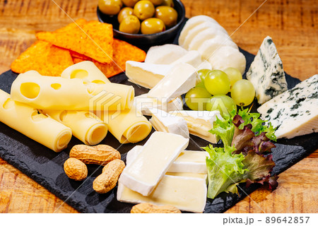 Assorted cheese on a black ceramic kitchen board with grapes, olives and nuts.Different types of cheeses on black board. Assorted cheese on a black ceramic kitchen board with grapes, olives and nuts.Different types of cheeses on black board. 89642857