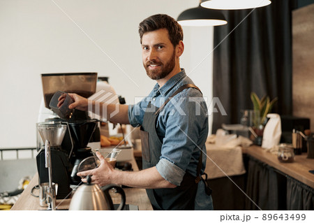 Barista pours coffee beans into the coffee machine tank for grinding Barista pours coffee beans into the coffee machine tank for grinding 89643499
