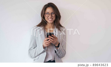 Businesswoman wearing glasses with mobile phone in hand standing in modern office 89643623