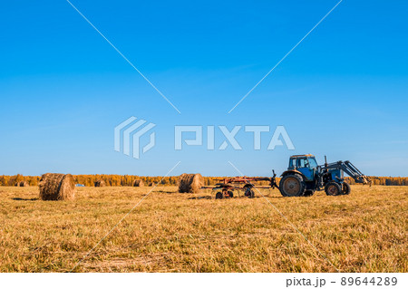 Tractor collecting haystacks in a field 89644289