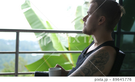 Young man drinking coffee sitting in balcony with exotic garden and sea view. 3840x2160 89645776