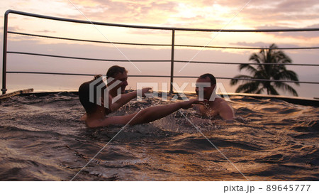 Happy friends swimming in pool splashing playfully enjoying summer vacation having fun celebrating summertime holiday at luxury hotel with ocean view sunset 89645777
