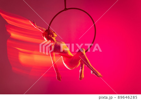 Young artistic girl, professional air gymnast training, performing isolated over pink background with mixed lights effect Young artistic girl, professional air gymnast training, performing isolated over pink background with mixed lights effect 89646285