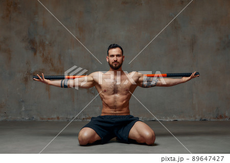 A ninja man holds on to a fighting stick and attacks close-up on gray studio background A ninja man holds on to a fighting stick and attacks close-up on gray studio background 89647427