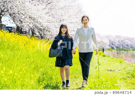 桜と菜の花に囲まれた通学路を歩く母親と高校生 89648714