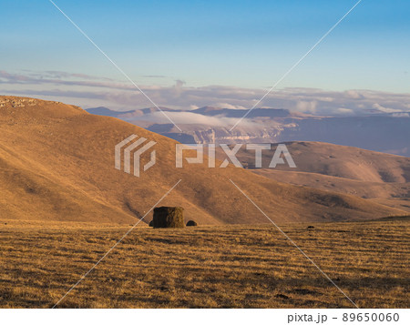 A rolled haystack in a field high in a mountain valley under a blue sky and low drifting clouds. The nature of the Caucasus 89650060