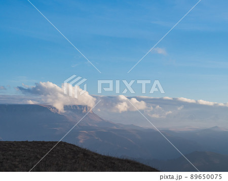 Hiding in the clouds under a bright blue sky is the Bermamyt plateau surrounded by a mountain valley on an autumn day Hiding in the clouds under a bright blue sky is the Bermamyt plateau surrounded by a mountain valley on an autumn day 89650075