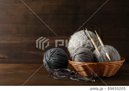 Multi colored balls of yarn with knitting needles in a wicker basket on a wooden background 89650205