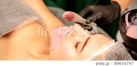 Beautiful young caucasian woman receiving an alginic mask to the face in beauty salon. Facial skin treatment 89650797