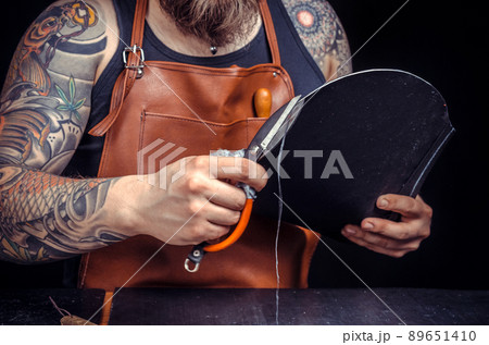 Currier of leather working with leather using crafting tools in his tanning shop Currier of leather working with leather using crafting tools in his tanning shop 89651410