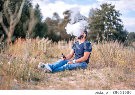Confident vape man enjoying an electronic cigarette in the forest. Alternative to smoking. 89651680