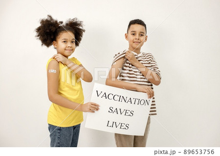 Boy and girl standing isolated on white background. Children have a band-aid on their shoulders after vaccination. Poster said that vaccination saved lives. 89653756