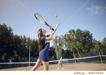 Tennis player woman focused during play. Caucasian woman playing tennis on the court outdoors. Woman wearing blue sport dress. 89654040