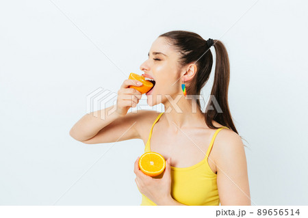 Cheerful woman in yellow top eating orange fruit 89656514