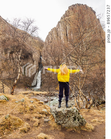 A woman with her face hidden under her hair stands on a rock in a rocky gorge with a waterfall in the background. Humorous image of a girl without a face 89657237