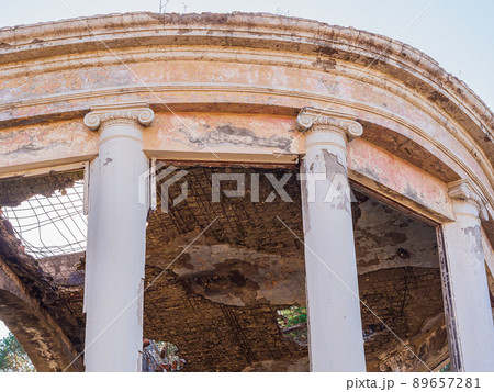 Fragment of a semicircular veranda of an abandoned dilapidated building in the Greek style with columns, large window openings and a broken roof 89657281