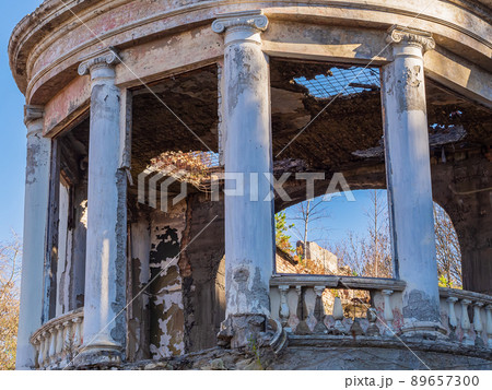 Semicircular fragment of an abandoned ruined restaurant with columns and balusters in the Greek style, overgrown with trees and with a broken roof 89657300