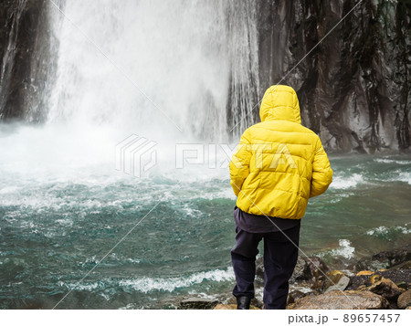 A woman takes a step into a turquoise mountain river into which a powerful icy stream of a waterfall falls. A woman takes a step into a turquoise mountain river into which a powerful icy stream of a waterfall falls. 89657457