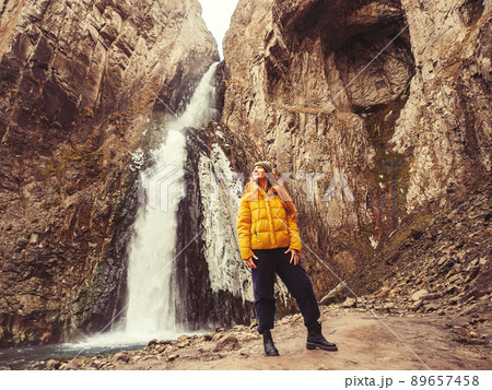 A woman looks up while standing against the background of an icy stormy waterfall flowing from a gorge of sheer rocks in the Caucasian highlands A woman looks up while standing against the background of an icy stormy waterfall flowing from a gorge of sheer rocks in the Caucasian highlands 89657458