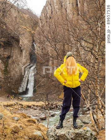A woman in a yellow jacket with hair instead of a face stands against the backdrop of rocks and a waterfall in an autumn mountain gorge. Comic image 89657536