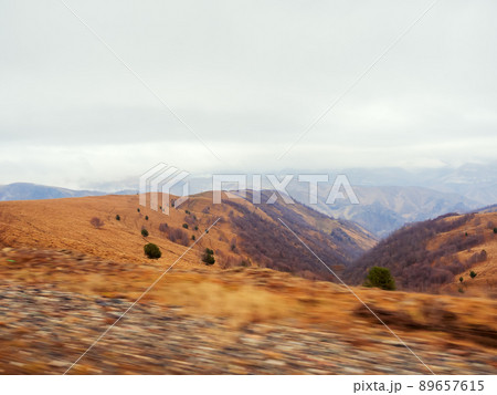 Autumn alpine valley covered with golden dry grass under low clouds. View from a passing car. Photo in motion 89657615